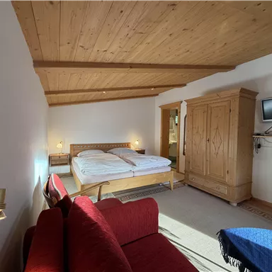 Ein helles Schlafzimmer mit Holzdecken und einem großen Bett. Es gibt eine rote Couch und einen Fernseher an der Wand.