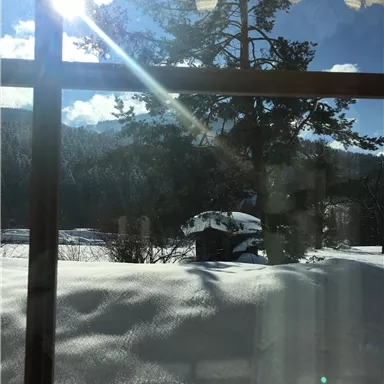 A sunny view from a window onto a snow-covered landscape. In the background, trees and a blue sky are visible.
