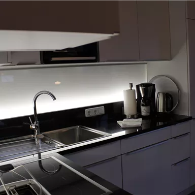 Eine moderne Küche mit schwarzen Arbeitsflächen und weißen Schränken. Es gibt einen Wasserhahn, Küchengeräte und eine elegante Beleuchtung.