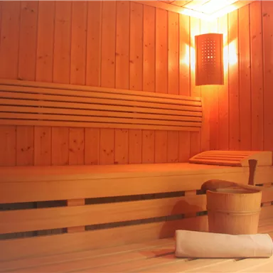A cozy sauna with wooden walls and warm lighting. In the room, there is a wooden bench and a container for water.