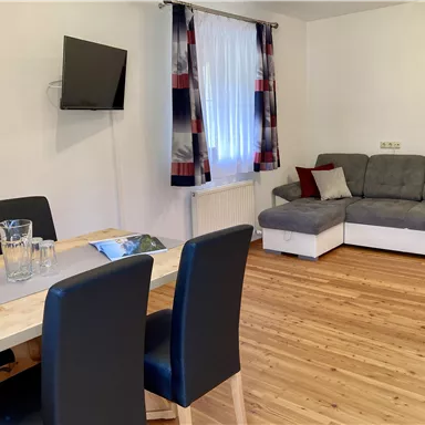 A cozy apartment with a dining area and a living room. The room has a bright atmosphere with a sofa and a television.