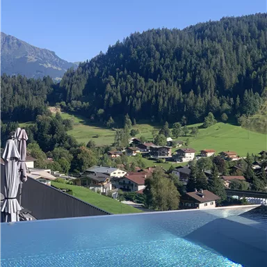 Ein schöner Blick auf ein Pool mit klarem Wasser, umgeben von grünen Bergen und Wäldern. Im Vordergrund sieht man ein ruhiges Dorf mit Häusern und Bäumen.