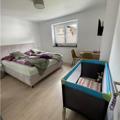 A modern bedroom with a large bed and a cozy blanket. In the corner, there is a children's bed and a small desk.