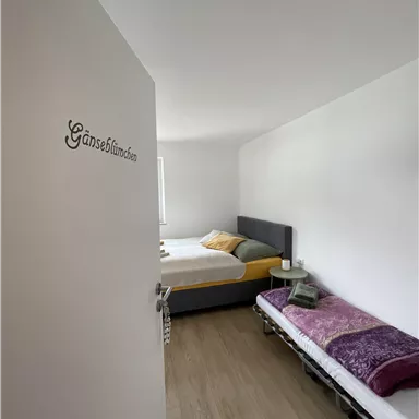 A bright room with two beds and simple furnishings.
There is a narrow space with a wooden floor and plain decor.