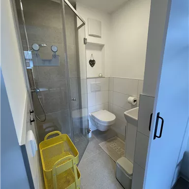 A modern bathroom with a transparent shower and a toilet. Yellow storage baskets are in the room.