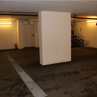Eine dunkle Garage mit freiem Platz und einzelnen Wänden. Einige Leuchten beleuchten den Raum.