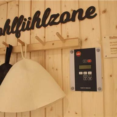 A wall with the inscription "Comfort Zone" and two hats hangs on a wooden stand. There is a digital control panel on the wall.