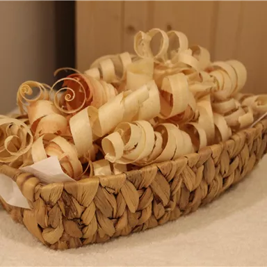 A woven basket full of wood shavings. The shavings are in various shapes and colors and appear decorative.