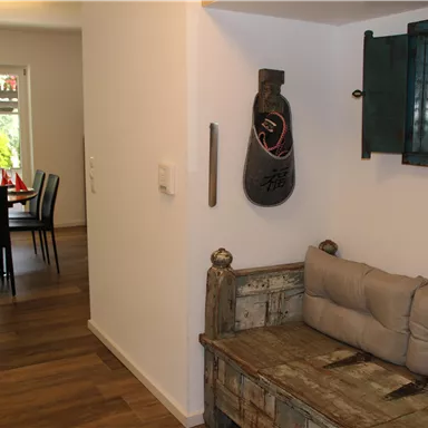 Ein einladender Flur mit einem alten Holzsofa und einem Dekorationsspiegel. Im Hintergrund ist ein Essbereich mit einem Tisch und Stühlen sichtbar.