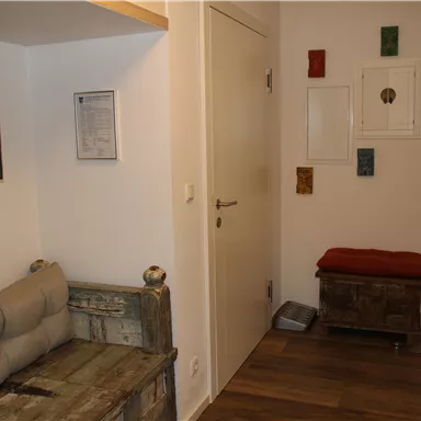 Ein gemütlicher Flur mit einem Holzsofa und hellen Wänden. An der Wand hängen dekorative Elemente in verschiedenen Farben.