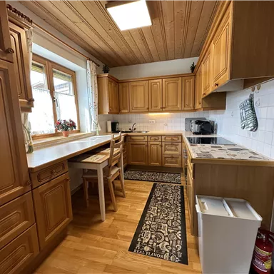 A cozy kitchen with wooden cabinets and a bright room. The table and chairs provide space for eating and lingering.