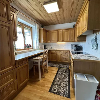 A bright kitchen with wooden cabinets and a large window. There is a small dining area and modern kitchen appliances.