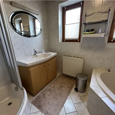 A modern bathroom with a shower cubicle, a bathtub, and a double sink. Bright tiles and windows create a friendly atmosphere.