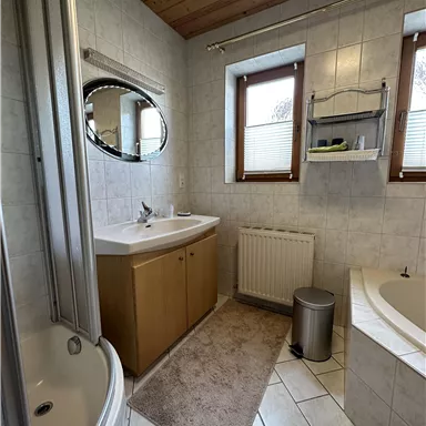 A bright bathroom with a shower, a bathtub, and a sink. Large windows provide plenty of daylight.