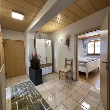 A bright hallway with a modern wardrobe and a chair. In the background, a bedroom is visible.