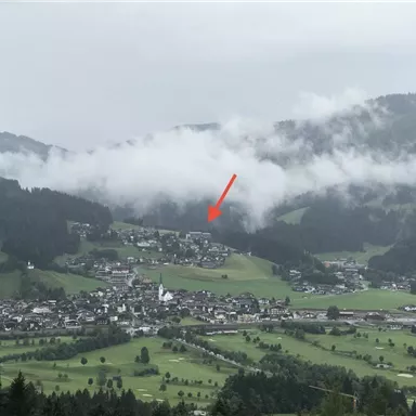 A picturesque valley with a small village, surrounded by green meadows and mountains. Clouds hang over the village, creating a mystical atmosphere.
