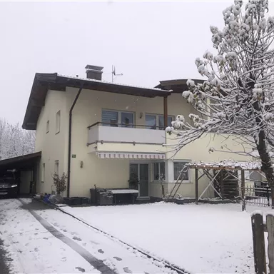 A house in the snow with a cozy carport. The garden is covered with fresh snow and it is cloudy.