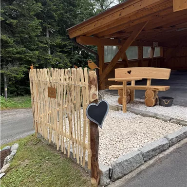 A beautiful entrance area with a wooden railing and a wooden bench. The ground is covered with pebbles and there is a lot of greenery in the surroundings.