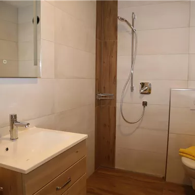 Ein modernes Badezimmer mit einer Dusche, einem Waschbecken und einer Toilette. Die Wände sind hell und die Einrichtung ist schlicht und elegant.