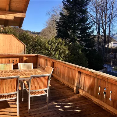 Ein gemütlicher Außenbereich mit Holzterrasse und Essgruppe. Umgeben von Bäumen und klarem Himmel.