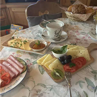 A set table with various breakfast delicacies. On it, cheese, ham, tomatoes, and a cup of coffee can be seen.