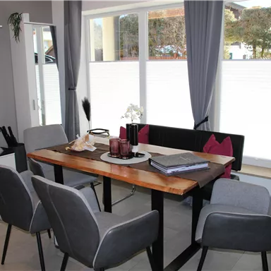 A modern dining area with a stylish wooden table and six gray chairs. Large windows provide plenty of natural light.