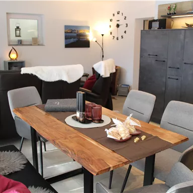 A modern living room with a large dining area. The wooden table is set with decorative elements and snacks.