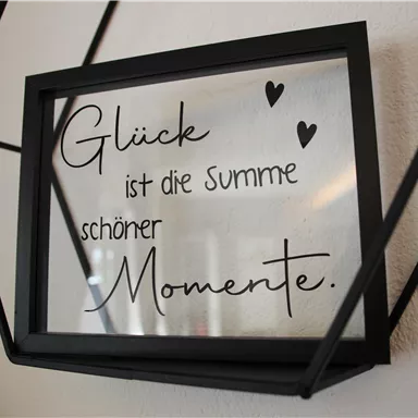 A framed glass picture with the inscription: "Happiness is the sum of beautiful moments." The frame is black and has a modern shape.