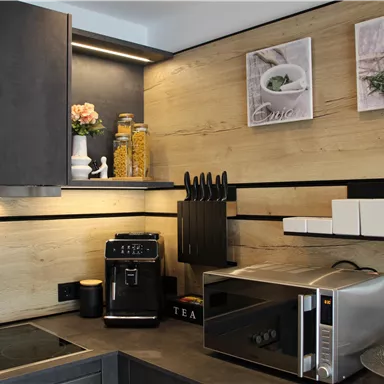 A modern kitchen with wooden panels and elegant appliances. On the countertop, there is a coffee machine, a microwave, and decorative elements.