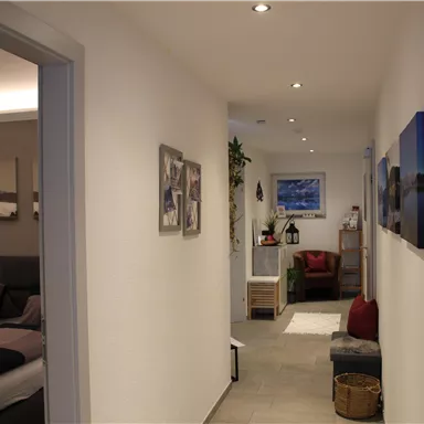 A bright hallway with modern pictures on the wall. On the left side, a bedroom is visible; the room feels inviting and cozy.