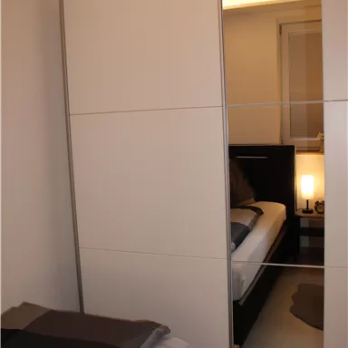 A modern bedroom with a white wardrobe and a bed. The light is dimmed and creates a cozy atmosphere.