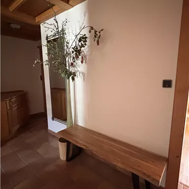 Ein heller Flur mit einer Holzbank und einem Spiegel. An der Wand wächst ein paar Zweige mit Blättern.