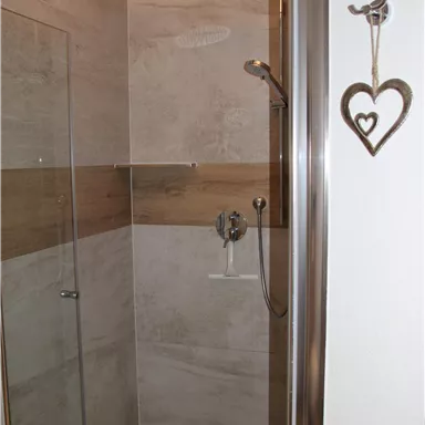 A modern shower cabin with neutral tiles and a wooden paneling. The space feels bright and inviting.