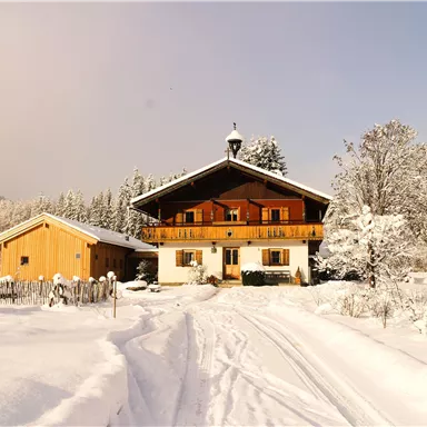 A cozy house in the snow with a large balcony. The surroundings are wintery and snowy, surrounded by trees.