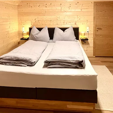 Ein gemütliches Schlafzimmer mit einem großen Bett und hellem Holzdekor. Die Atmosphäre ist warm und einladend, mit sanfter Beleuchtung.