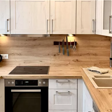 Eine moderne Küche mit Holzverkleidung und weißen Schränken. Sie verfügt über Kochfelder, einen Backofen und eine Spüle.