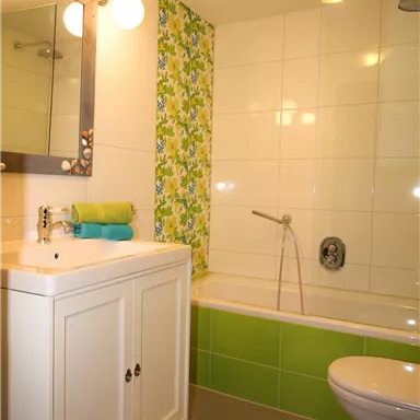 Ein modernes Badezimmer mit einer Badewanne und einer Toilette. Die Wände sind mit weißen Fliesen und grünen Akzenten dekoriert.