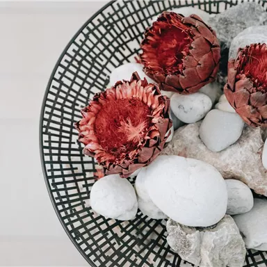 A decorative bowl with red dried flowers and white stones. The arranged elements give a natural and elegant look.