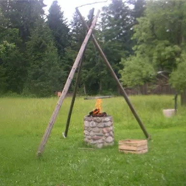 A cozy campfire on a stand in a green meadow. In the background, trees and a chicken are visible.