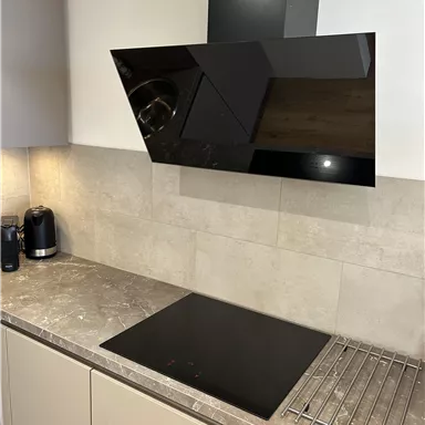 A modern kitchen with a black ceramic cooktop and an elegant range hood. The workspace is in neutral shades and has a clean, minimalist look.