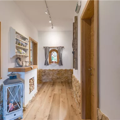 An inviting hallway with wooden details and a warm atmosphere. Decorative elements and a window with curtains can be seen on the walls.