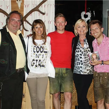 A group of five people in traditional Bavarian attire in a cozy restaurant. They are smiling and posing for a photo.