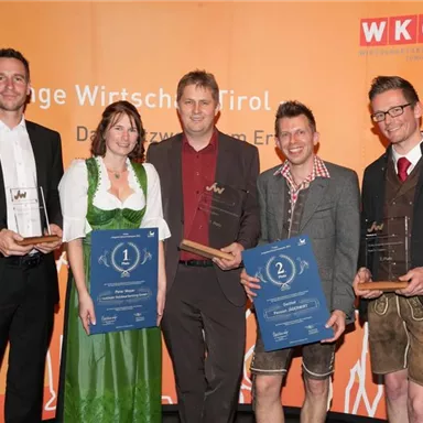 A group of four people is standing on a stage. They are holding awards and plaques in their hands, while an orange banner from WKO is visible in the background.