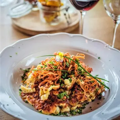A plate of delicious roasted potatoes, garnished with fresh chives and crispy onions. In the background, a glass of red wine and several small dishes are visible.