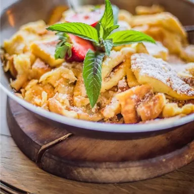 A plate of delicious Kaiserschmarrn, garnished with fresh strawberries and mint. The sweet, fluffy dish is placed on a wooden board.