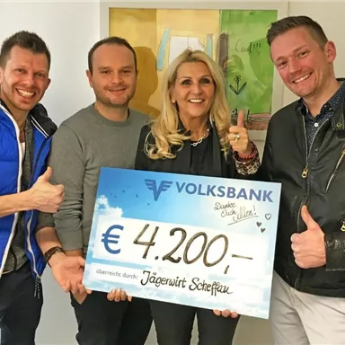 Four people pose smiling with a large check for 4,200 euros from the Volksbank. The check is presented to support an organization or project.
