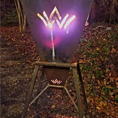 Ein metallischer Feuerplatz in einer dunklen Umgebung. Die Struktur hat leuchtende Verzierungen in Form eines W.
