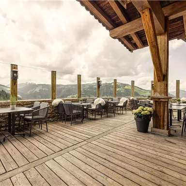 A terrace with a wooden floor and stylish furniture offers a view of the mountains. The sky is overcast, creating a cozy atmosphere.