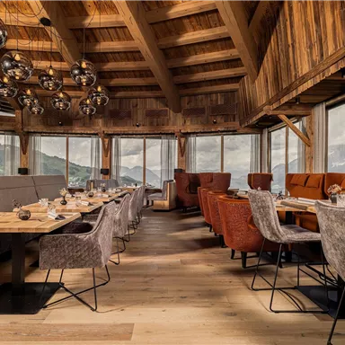 A modern restaurant with wood paneling and large windows. The tables are elegantly set and offer a view of the surrounding landscape.