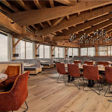 A modern restaurant with a wooden ceiling and large windows. The tables are elegantly set and the chairs are orange.